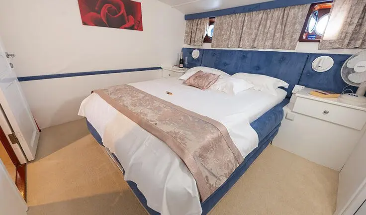 Arum cabin with two beds, brown comforters, blue headboard, and a small window