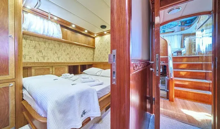 Interior view of a yacht cabin with a bed, wooden door, and shelves