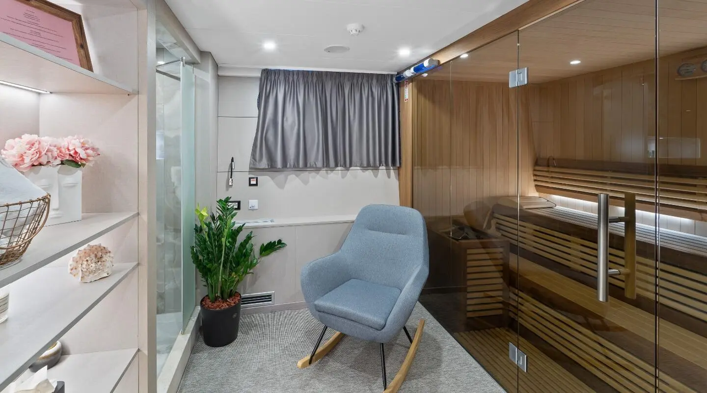 Interior lounge area of Freedom yacht with blue armchair, plants, and gray curtains