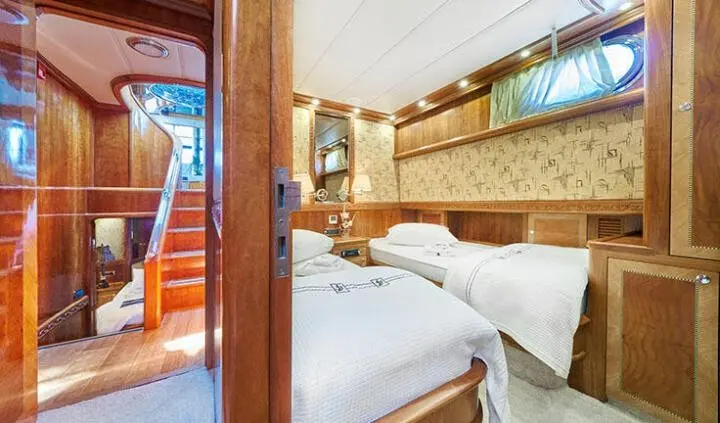 Two twin beds in a polished cabin with wood cabinetry and porthole