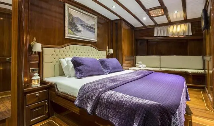 Master cabin with two beds, purple bedspreads, wood paneling, overhead ceiling beams