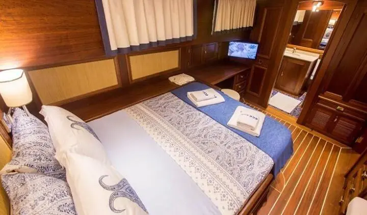 Yacht cabin with double bed, blue pillows, wooden walls, and carpeted floor