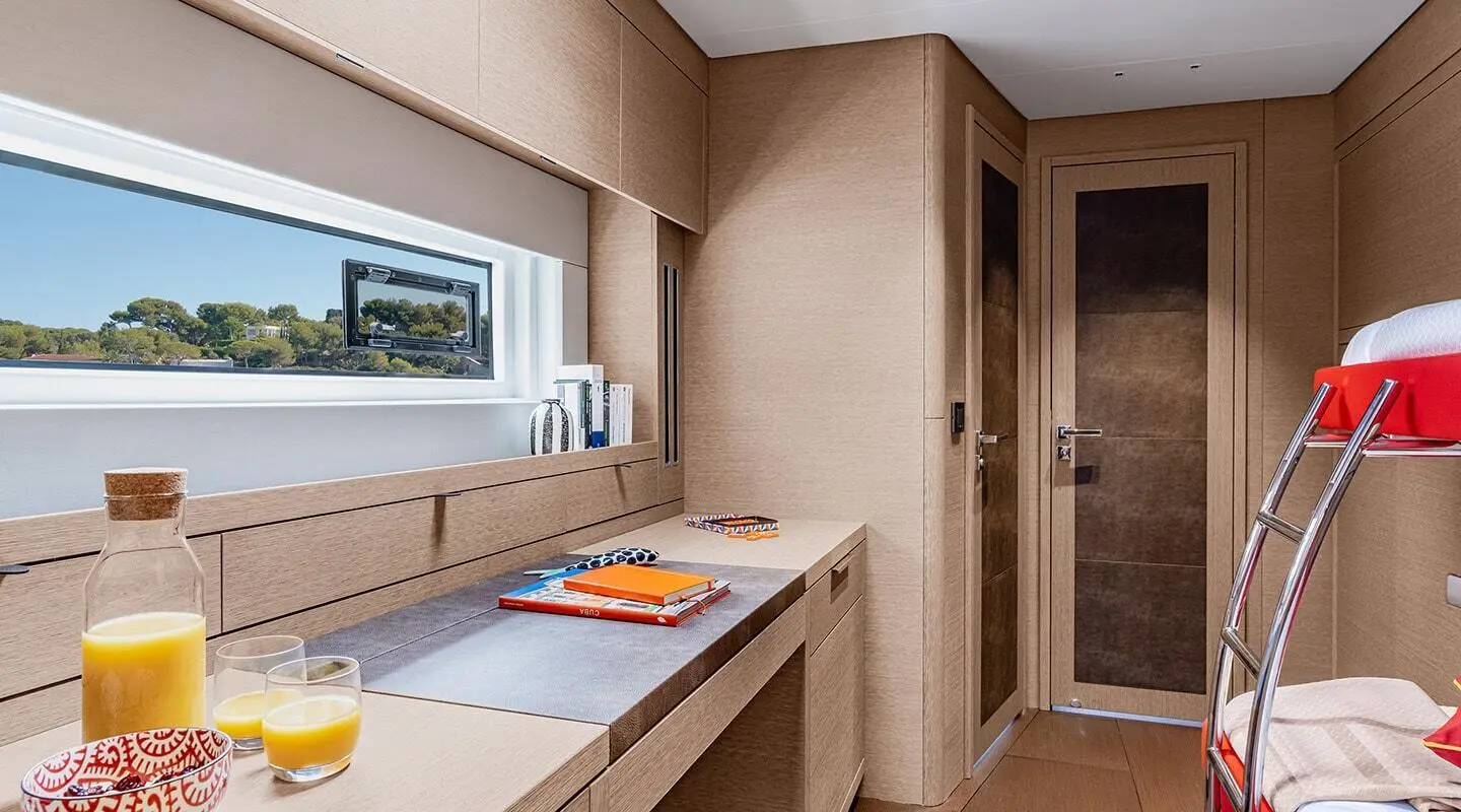 Interior of a luxury sailing yacht showing a light wood galley with counter and hatch, windows, and a door to a cabin