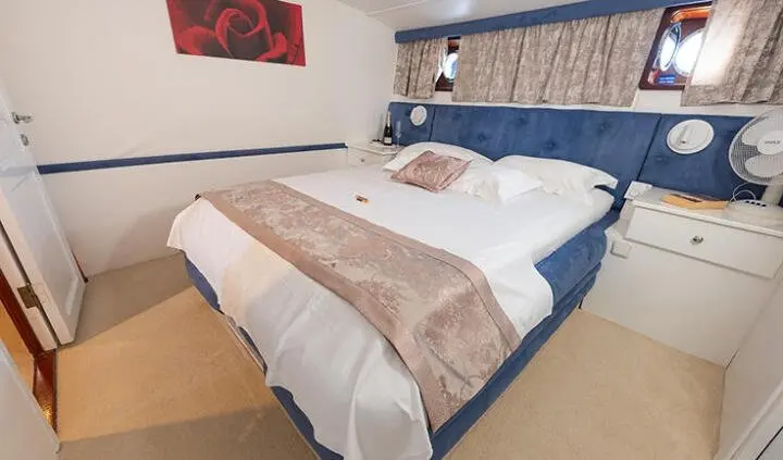 Aurm yacht cabin with a large double bed, beige bedding, and blue headboard