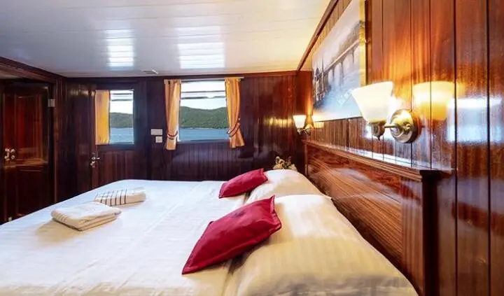 Yacht Cesarica cabin with wooden paneling, two beds, red pillows, bedside lamps