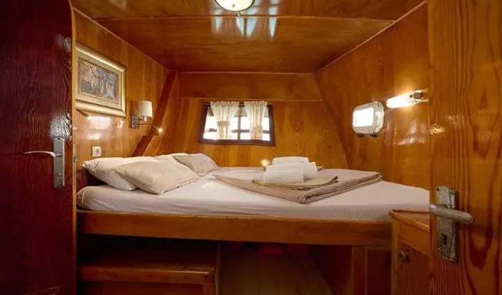 A cozy yacht master cabin with a large bed, wooden panels, and porthole windows
