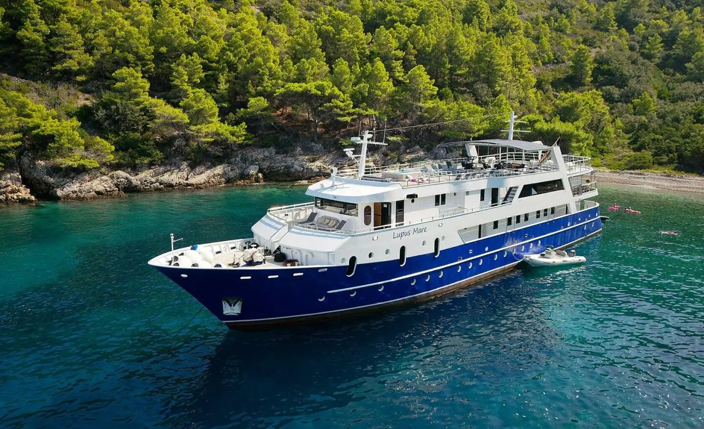 Lupus Mare yacht anchored near rocky shoreline with forest backdrop