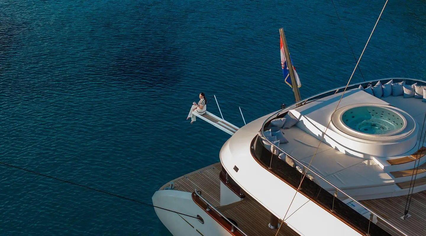 Person sitting on a platform over the sea next to a large yacht with a round pool on deck