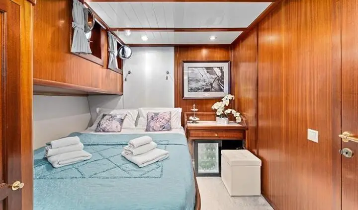 Smart Spirit yacht cabin with double bed, teal linens, wooden paneling, and compact seating