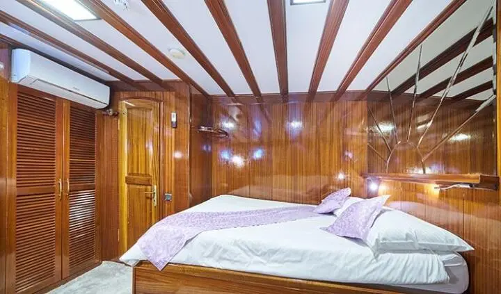 Stella Maris master cabin with wooden panel walls and large bed, sunlight through ceiling beams