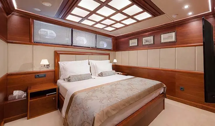 Lady Gita cabin with king bed, beige bedding, wooden paneled walls, porthole windows