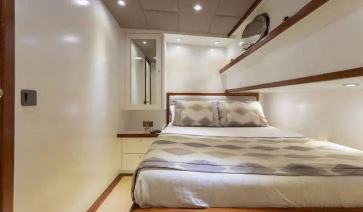 Two single beds in a beige cabin with a shared headboard and overhead lighting