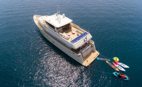 The Grace yacht's upper deck and aft area visible in open water; seating and cushions on the deck, rear platform, and attached water toys including kayaks and a jet ski