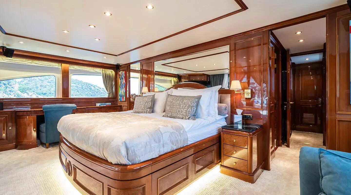 Amadea yacht bedroom with a large bed, wooden cabinetry, and porthole window