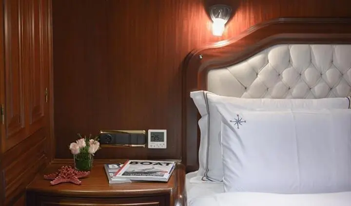 Master cabin with king bed, white pillows, wood paneling, bedside table