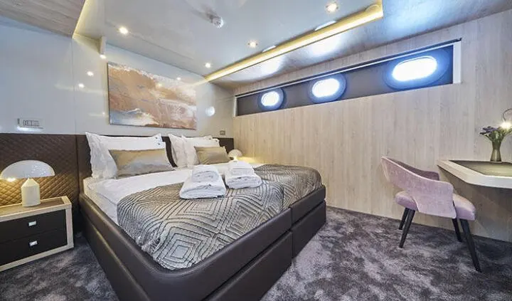 Yacht cabin with two neatly made beds, wooden walls, soft lighting, and patterned rug