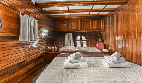Cozy wooden cabin interior with a bed, towels folded on mattress, and warm lighting