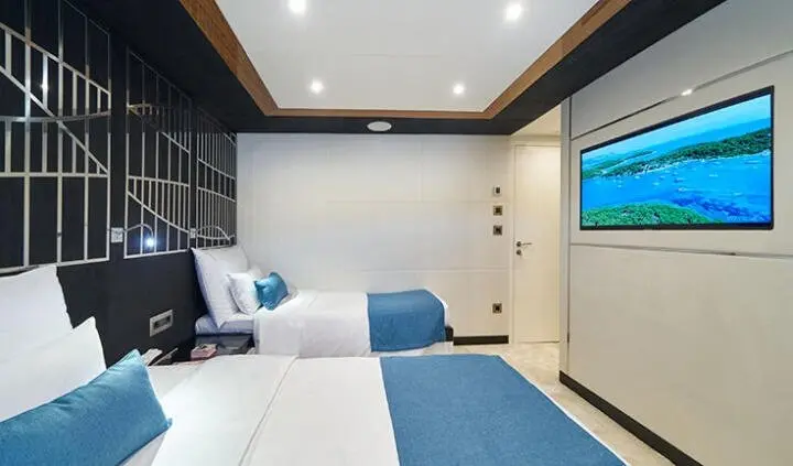 Twin cabin with two single beds, blue throws, and a flat-screen TV