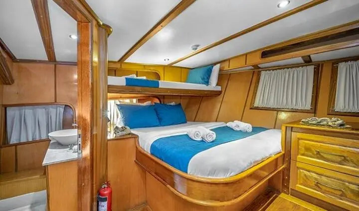 Interior of a yacht cabin with three beds, blue and white bedding, wooden walls