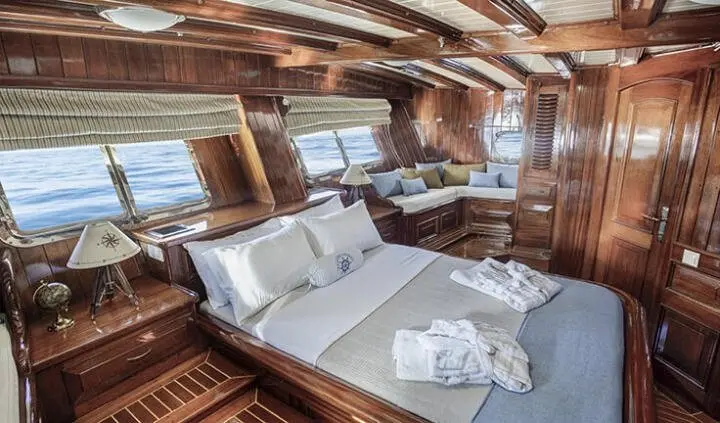 Master cabin with large bed, white linens, wooden paneled interior, windows