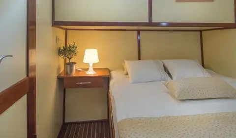 Twin bed cabin on yacht with wooden paneling, bedside lamp, and nightstand