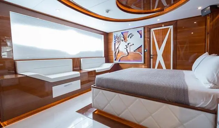 Yacht cabin interior with king bed, ensuite door, wooden accents, seating area