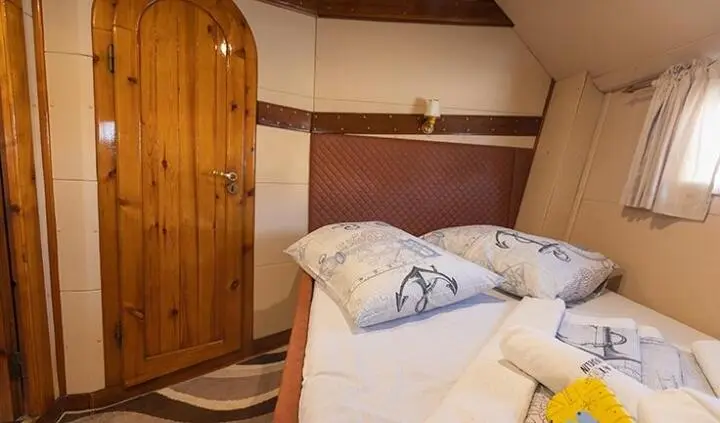 Cozy yacht cabin with double bed, pillows, wooden wardrobe, and soft lighting