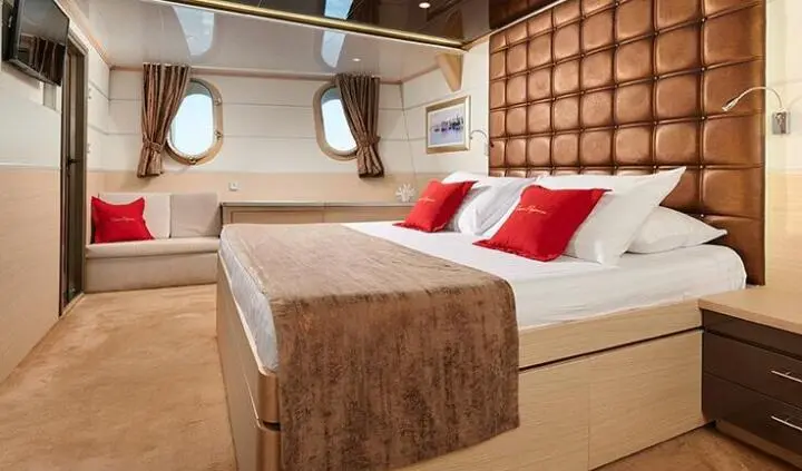 Queen Eleganza cabin bed with white linens, brown blanket, red pillows on a large bed