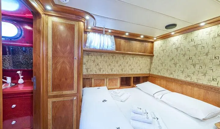 Lotus cabin interior with neatly made bed, wooden cabinets and porthole