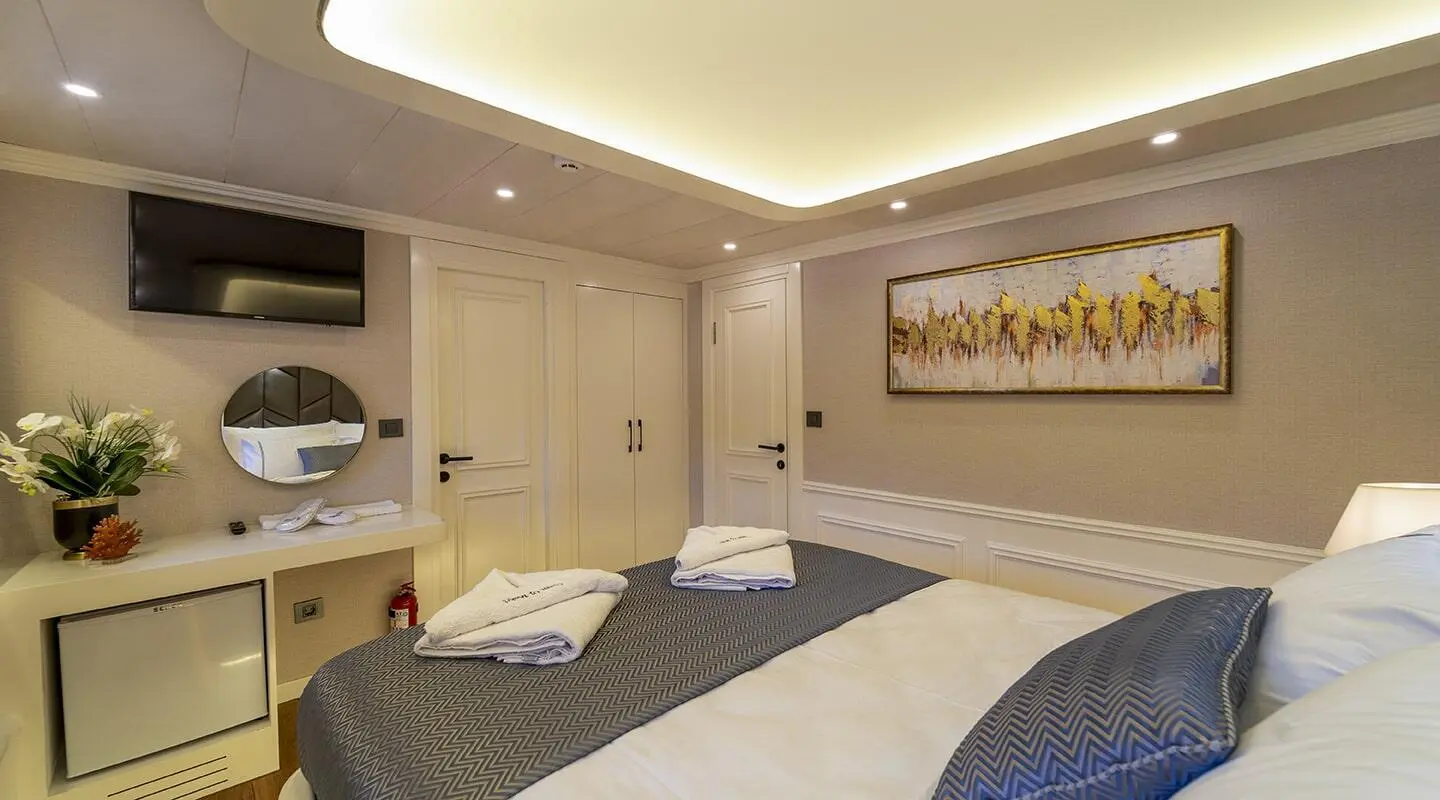 Interior yacht cabin with twin beds, built-in storage, soft lighting, and framed wall art
