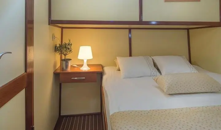 Twin bed cabin with beige bedding, wooden nightstand, lamp, and built-in overhead storage