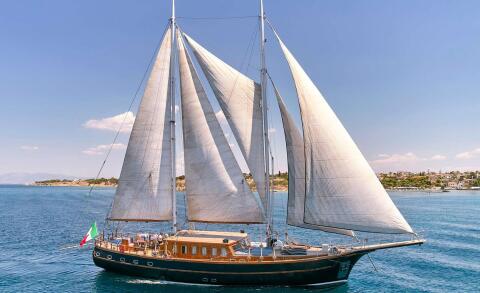 Myra sailing yacht with tall sails on calm blue waters near a coastal town