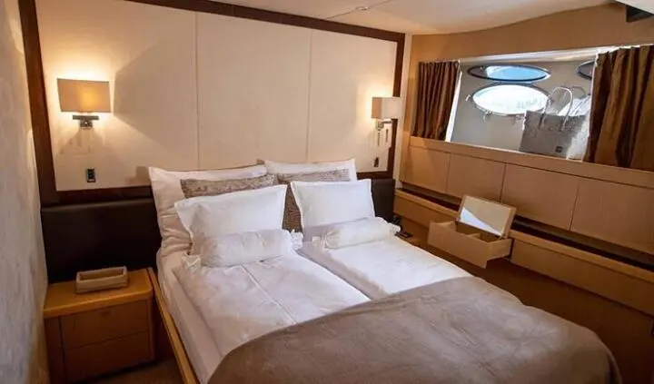 Master cabin with king bed, white bedding, wooden furniture and porthole