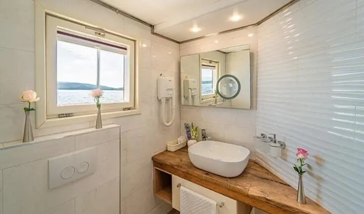 Akin master cabin with a round vessel sink on a wooden vanity and porthole view