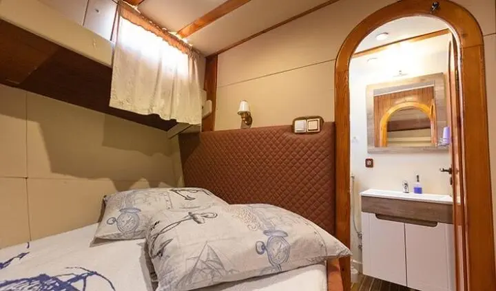 Cozy guest cabin on Gardelin yacht with bed, pillows, and porthole window