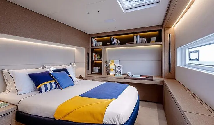 Master cabin with king bed, blue-yellow throw, built-in shelves, and ensuite