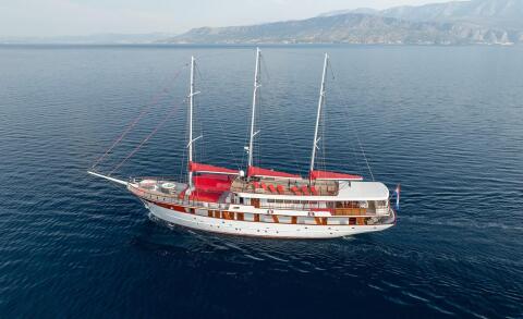 Luxury sailing yacht Barbara on the open sea with red sun loungers on the deck and masts visible