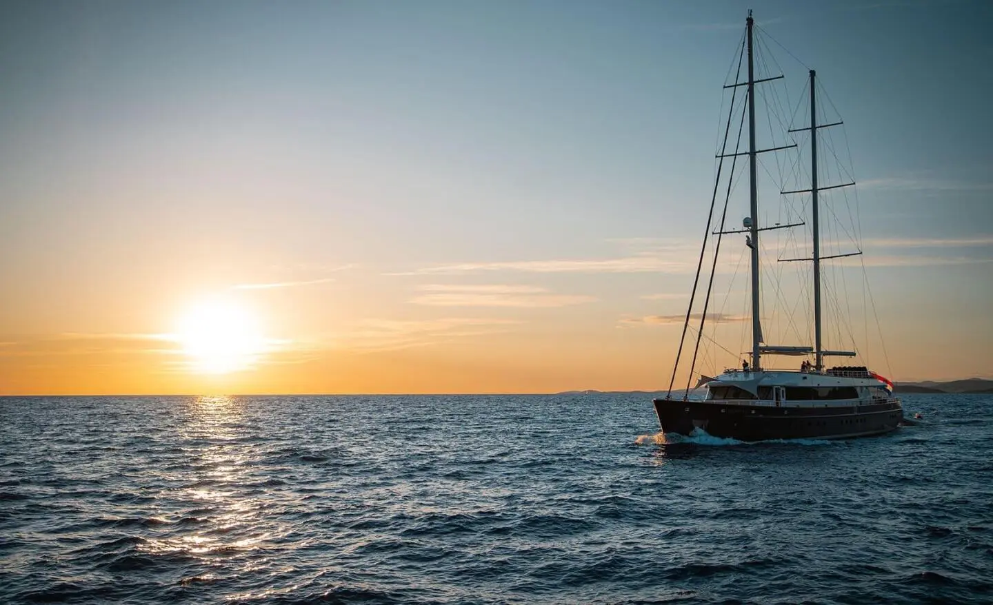 Dalmatino yacht at sunset with sailboat silhouette on calm sea
