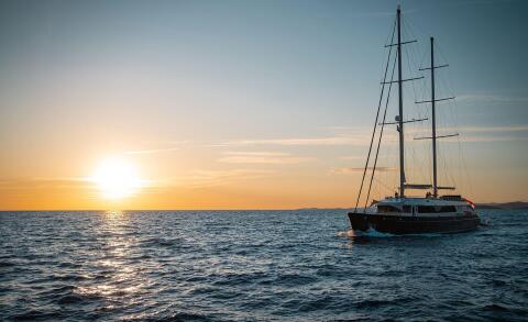 Dalmatino luxury yacht sailing at sunset on calm sea, two masts, sleek hull, golden horizon