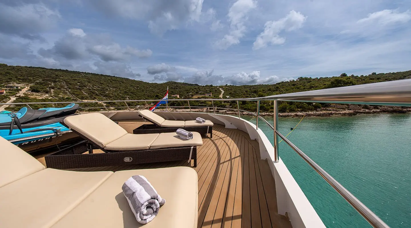Sunlit luxury yacht deck with tan sails and open seating along the bow