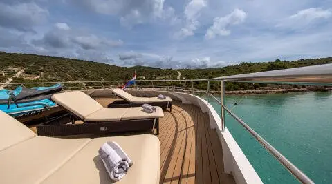 Sunlit luxury yacht deck with tan sails and open seating along the bow
