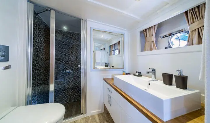 Maske yacht cabin interior with glass shower, dual vanity sink, and porthole window
