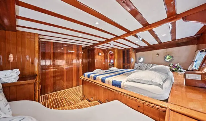 Eleganza yacht cabin with polished wood panels, a large double bed, and nautical decor