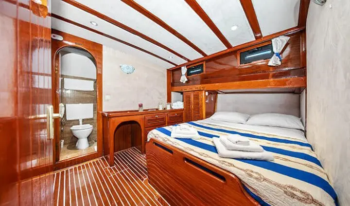 Interior of a yacht cabin with wood cabinetry, bunks, and blue-striped bedding