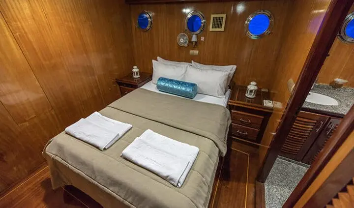 Cozy yacht cabin with king bed, wooden walls, and bedside lamps