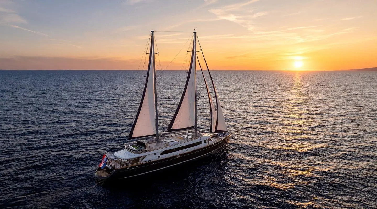 Dalmatino sailing yacht with sails up on calm sea at sunset