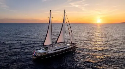 Dalmatino sailing yacht with sails up on calm sea at sunset