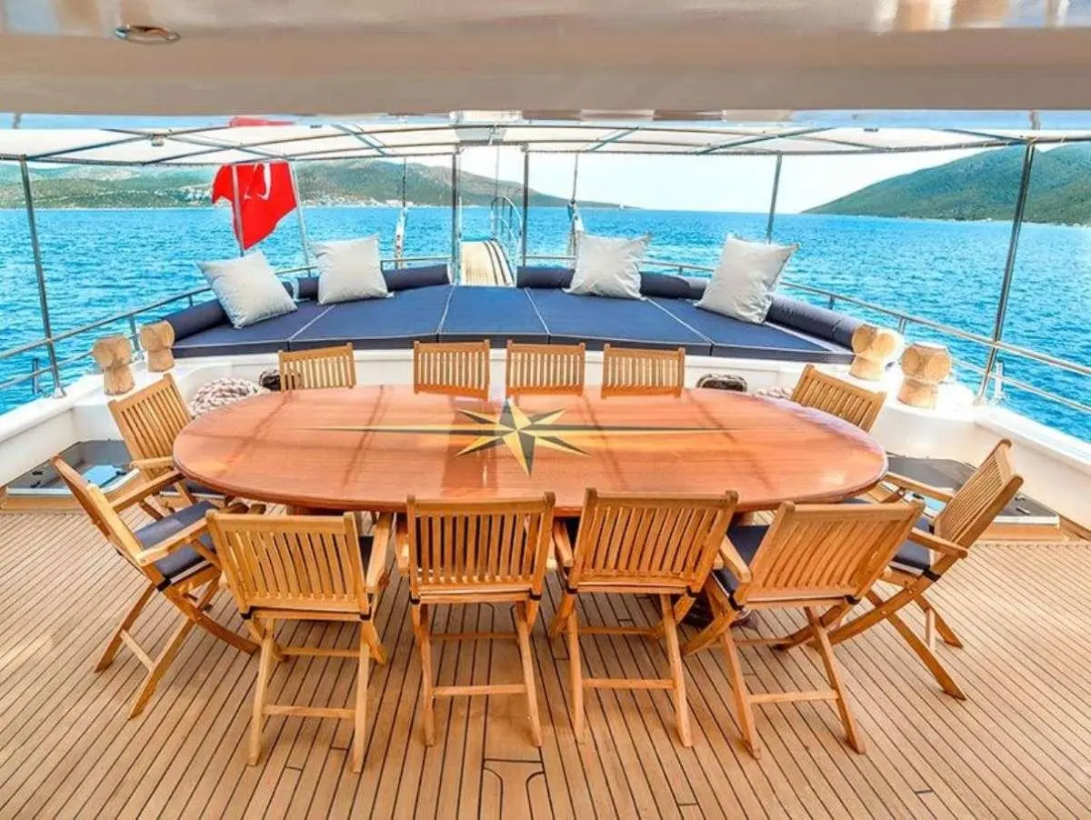 Bella Mare yacht deck with oval wooden dining table and wooden chairs near blue sea
