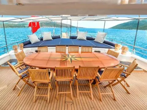 Bella Mare yacht deck with oval wooden dining table and wooden chairs near blue sea
