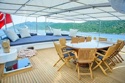 Bella Mare yacht deck with wooden dining table and lounge seating under a canopy